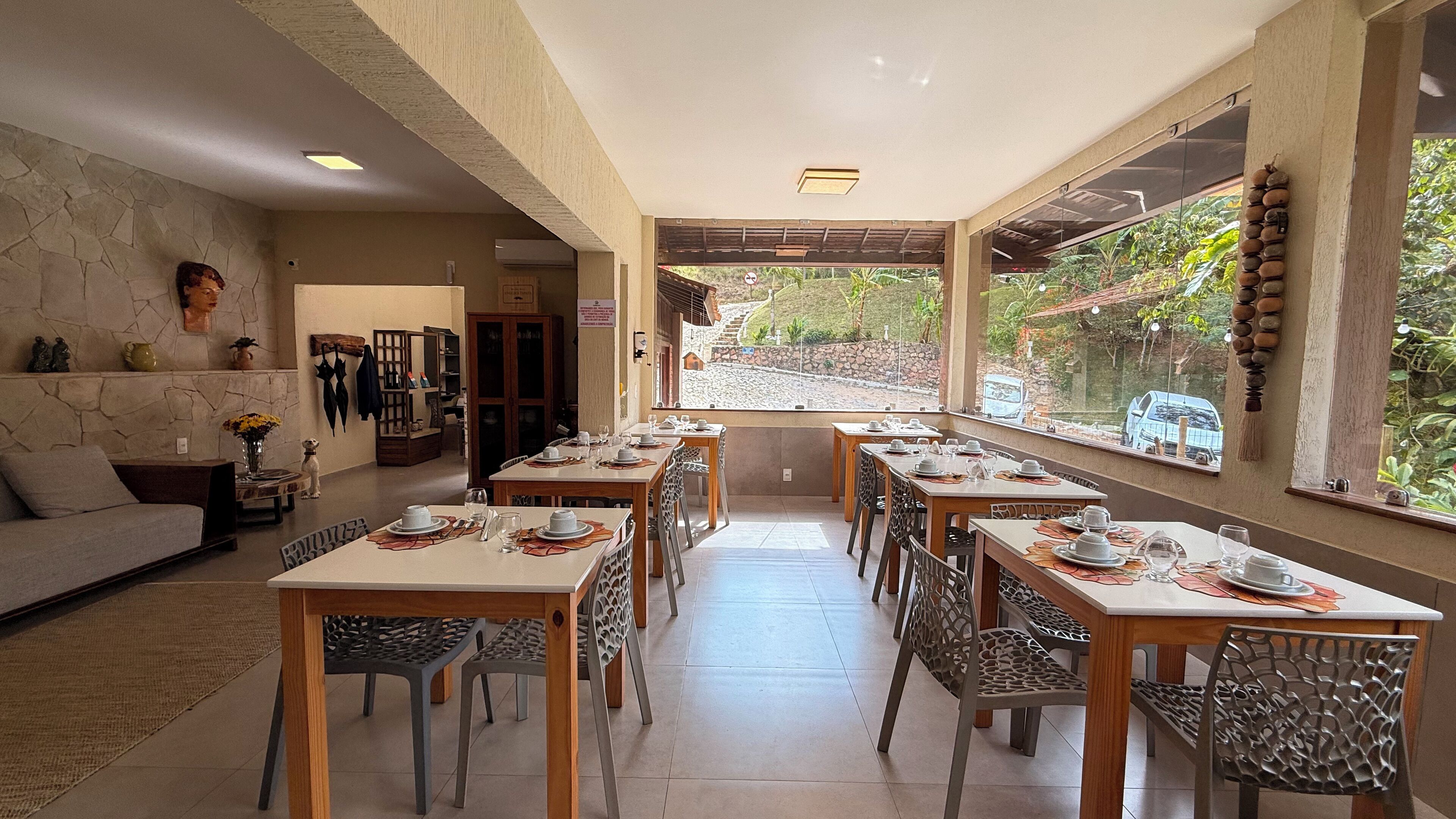 A dining area with tables set for a meal, a stone wall, and a view of a garden.