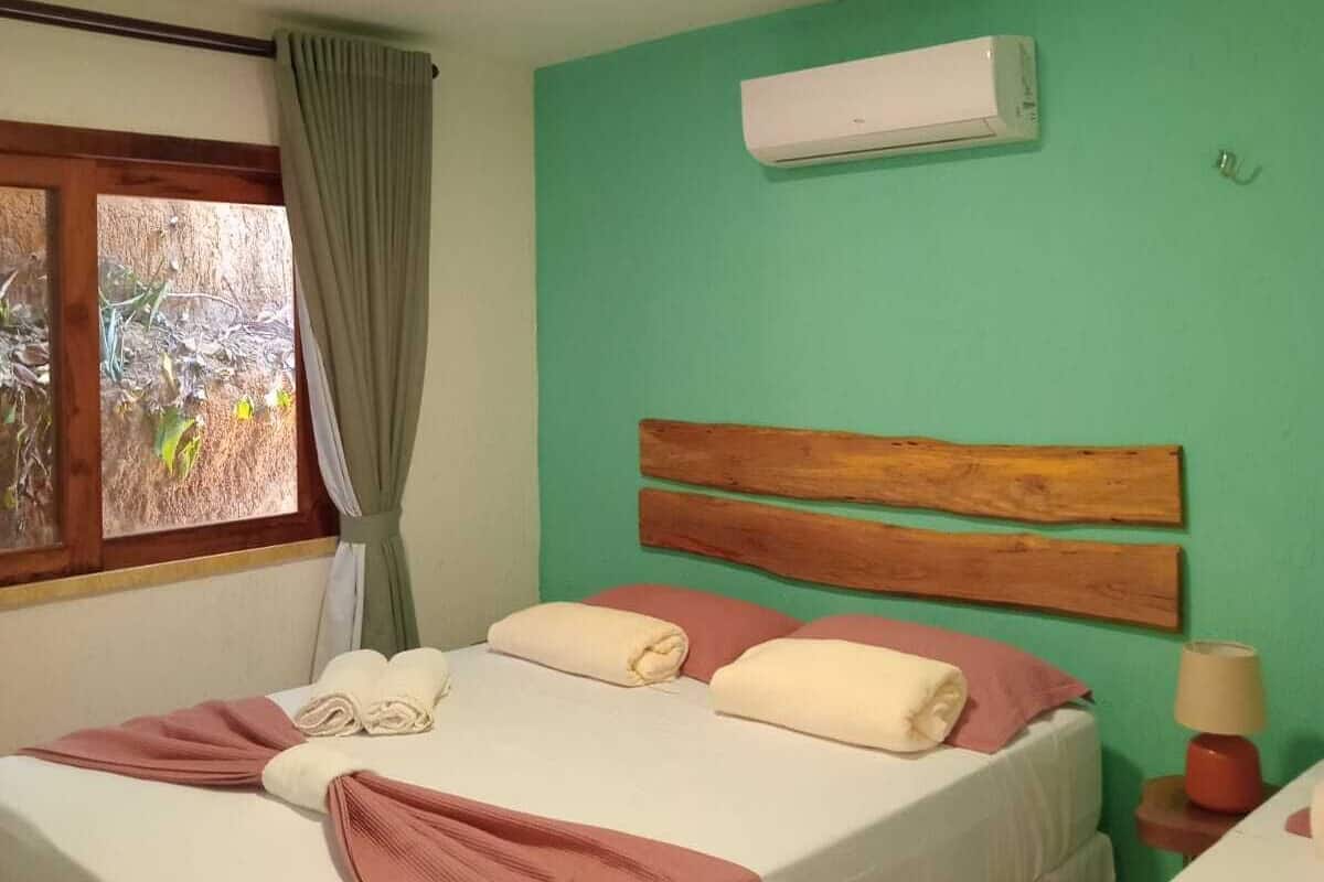 A bedroom with two beds, an air conditioning unit, a window with curtains, and a bedside lamp.