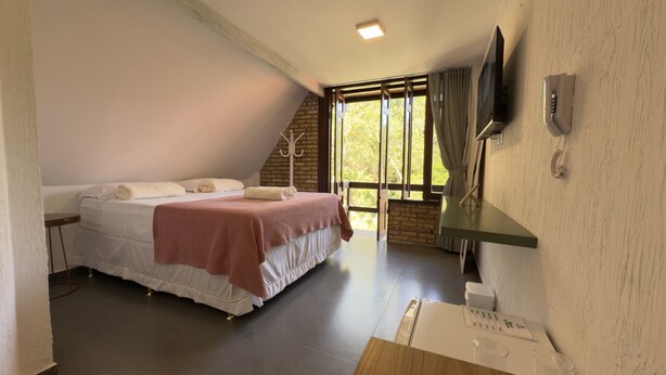 Un dormitorio con cama, mesita de noche, televisor montado en la pared y ventana con cortinas.