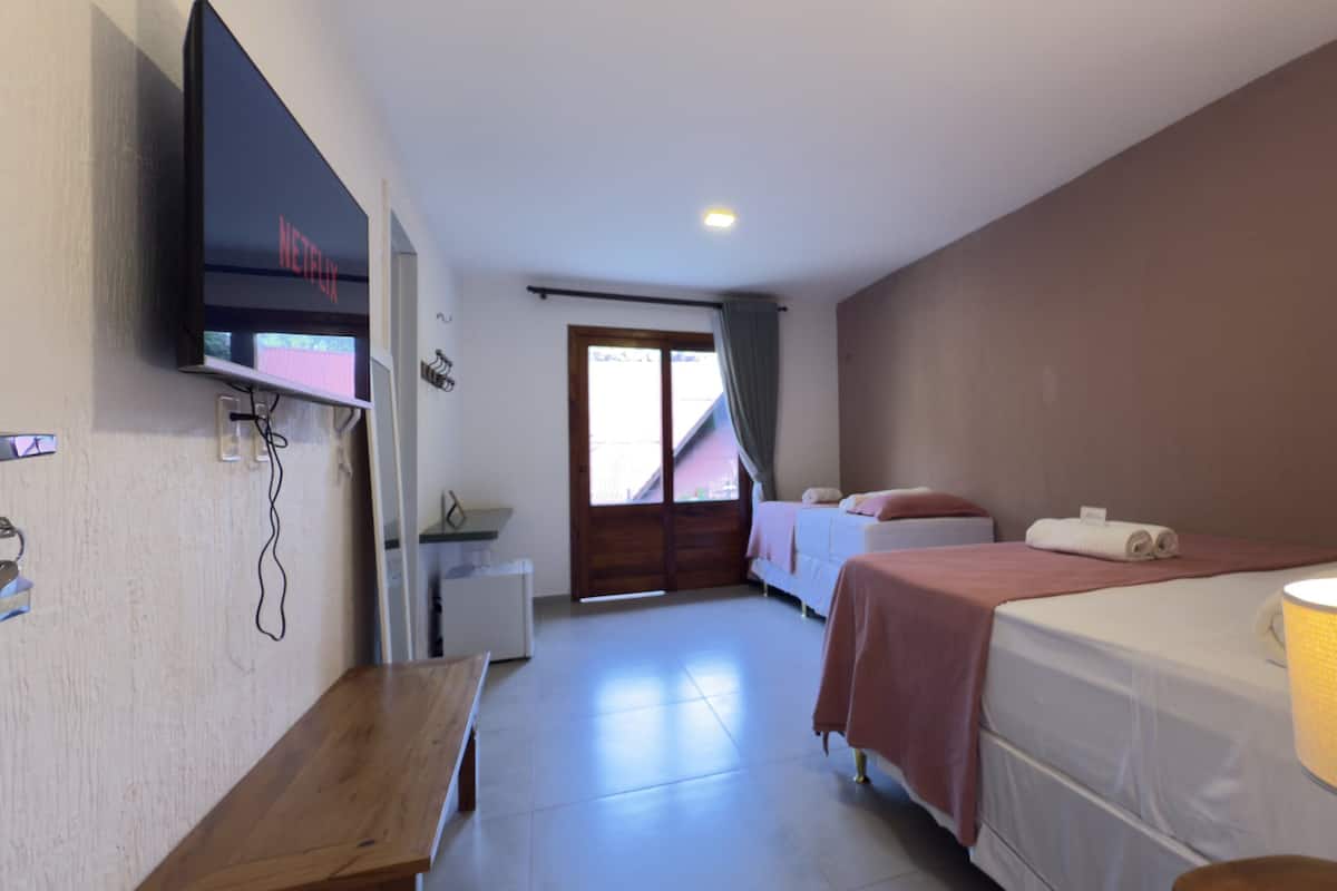 A hotel room with a bed, a desk, a TV mounted on the wall, and a window with curtains.