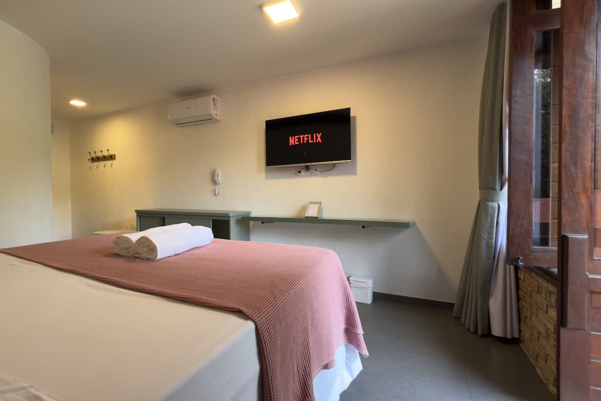 A hotel room with a bed, a desk, a TV mounted on the wall, and a door to the right.