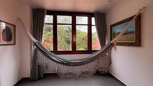 Una habitación con un ventanal grande, una hamaca, un cuadro enmarco y una fotografía en la pared.