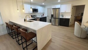 Cocina moderna con una isla central, taburetes de bar, electrodomésticos de acero inoxidable e iluminación colgante.