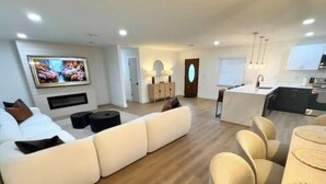 Una sala moderna con un sofá modular, un comedor con mesa redonda y una cocina al fondo.
