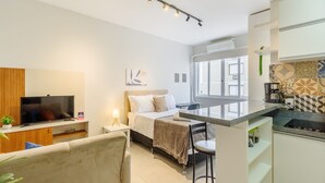 A modern hotel room with a bed, a TV, a desk, and a kitchenette. - Studio 750m From Redencao Park Hpn0618 (Porto Alegre)