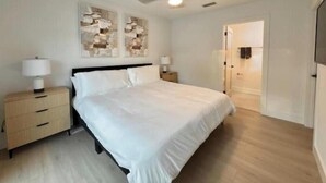 Un dormitorio con una cama, dos mesitas de noche, un ventilador de techo y una puerta que da a otra habitación.