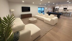 Una sala de estar moderna con una mesa de billar, un conjunto de sofás y un televisor de pantalla plana.