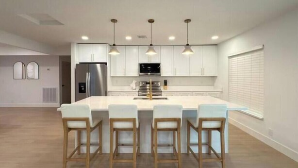 Una cocina moderna con armarios blancos, un refrigerador de acero inoxidable y una isla central con taburetes de bar.