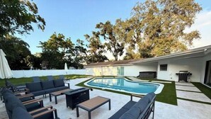 Un patio exterior con piscina, zona de estar y área de barbacoa cubierta.