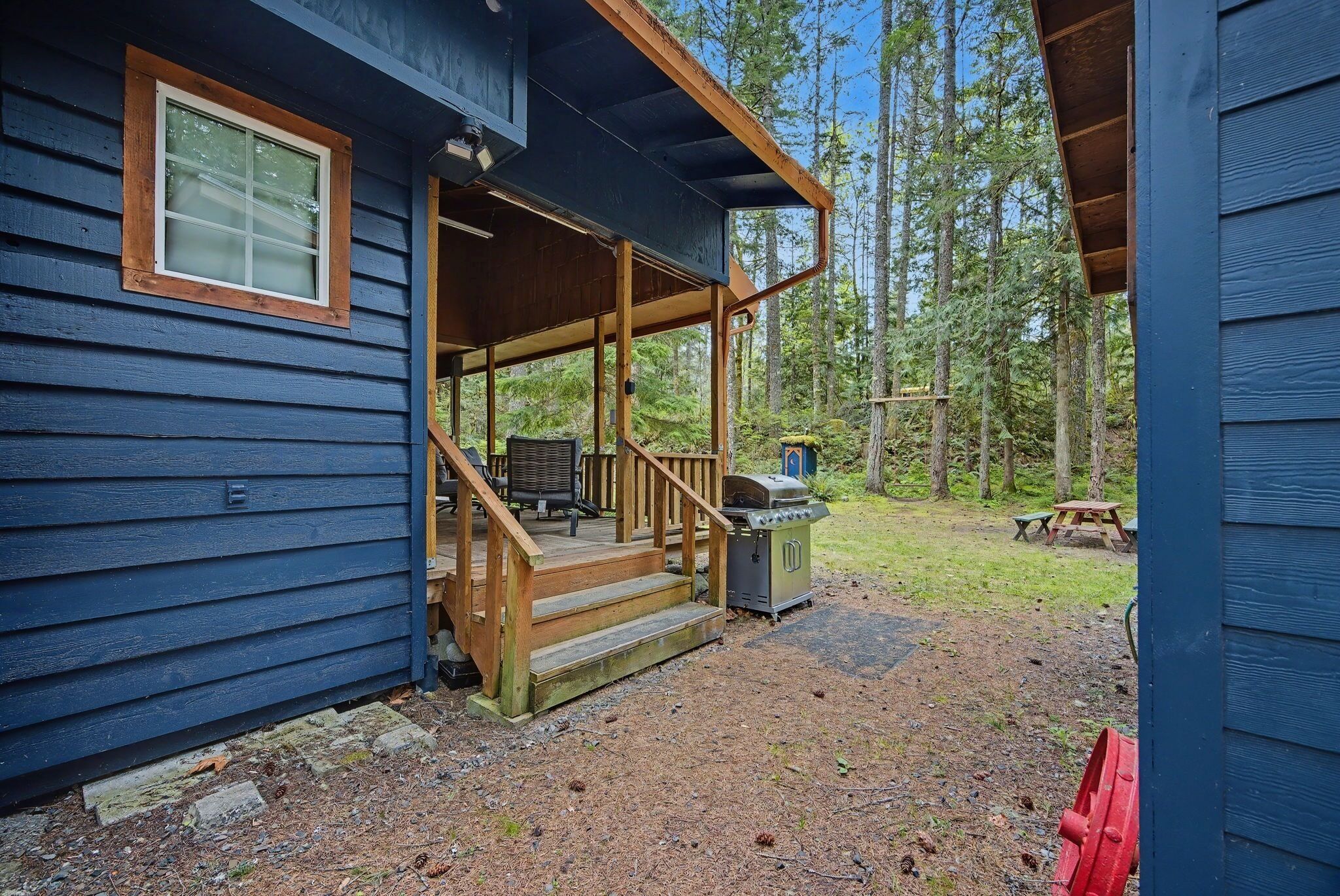 Eine Holzhütte mit einer Holzterrasse, einem Grill und einem Picknicktisch in einer Waldlandschaft.