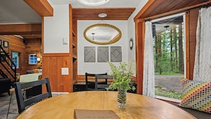 A wooden interior with a dining table, chairs, a vase with a plant, a mirror, and a view of a forest through a glass door. - Mt Hood Cabin Sanctuary with Hot Tub, Pets Welcome (Mount Hood Village)