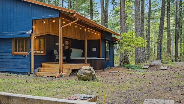 A blue cabin with a wooden porch, a small deck, and a view of the forest. - Mt Hood Cabin Sanctuary with Hot Tub, Pets Welcome (Mount Hood Village)