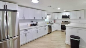 A modern kitchen with white cabinets, stainless steel appliances, and a wooden floor.