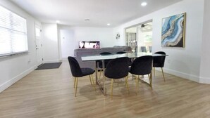A modern dining area with a white table, four black chairs with gold legs, and a large painting on the wall.