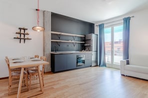Eine moderne Küche mit eingebauten Geräten, ein Essbereich mit Holztisch und -stühlen sowie eine große Schiebeglastür zum Balkon.