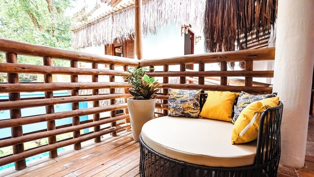 Um deck de madeira com um sofá redondo de vime, um vaso de planta e uma estrutura de telhado de palha.
