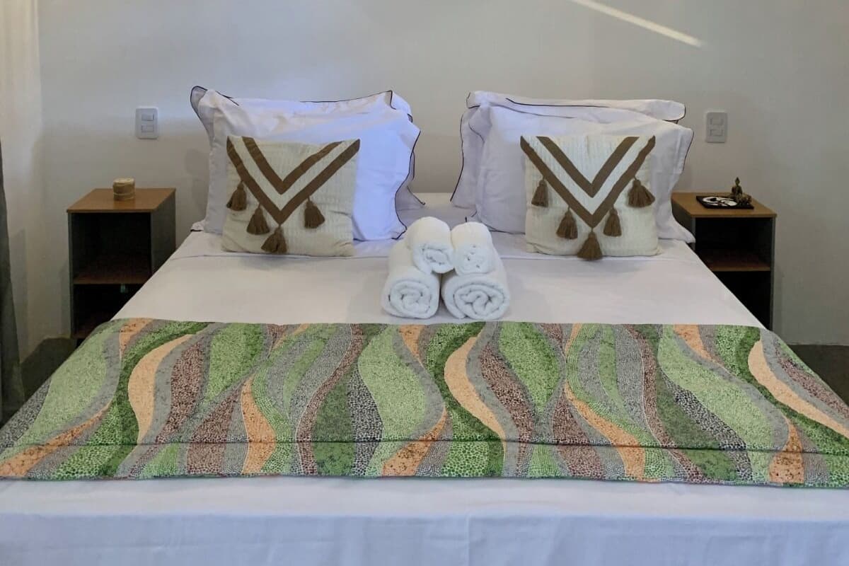 Una habitación de hotel con cama, dos mesitas de noche, un cuadro y dos apliques de pared.