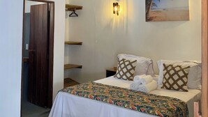 Quarto com cama, luminária na parede, um quadro e porta de madeira.