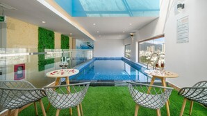 Una piscina interior con paredes de vidrio, césped artificial y vistas a la ciudad.