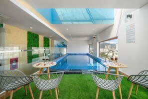 Una piscina interior con paredes de vidrio, césped artificial y vistas a la ciudad.
