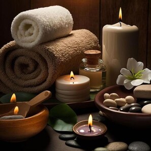 A spa setting with a rolled towel, candles, a wooden bowl, and stones. - Sapphire Hotel (Da Nang Municipality)