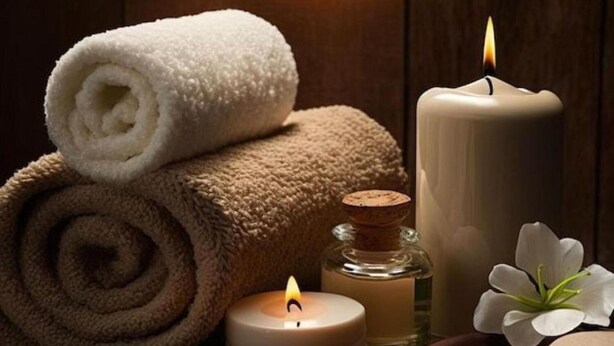 Un entorno de spa con una toalla enrollada, velas, un cuenco de madera y piedras.