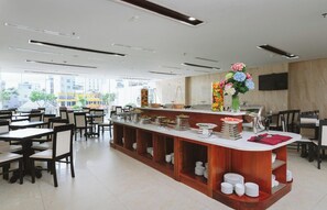 A restaurant with a central bar, multiple dining tables, and a view of buildings outside. - Sapphire Hotel (Da Nang Municipality)