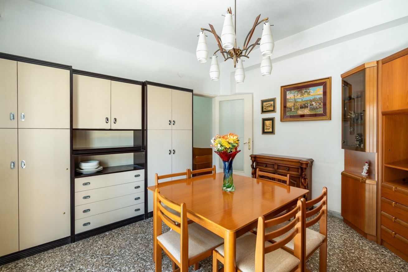 A dining area with a wooden table and chairs, a vase with flowers, and a chandelier.