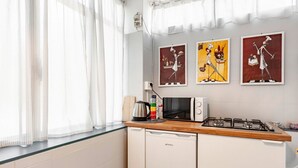 Een keuken met een magnetron, gasfornuis en koffiezetapparaat. Drie kunstwerken hangen in lijstjes aan de muur.