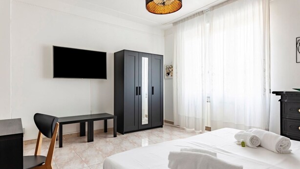 Een hotelkamer met een bed, een bureau, een stoel, een kledingkast en een televisie aan de muur.