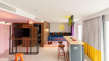 A modern hotel room with a living area, a kitchenette, a TV, and a bar area.