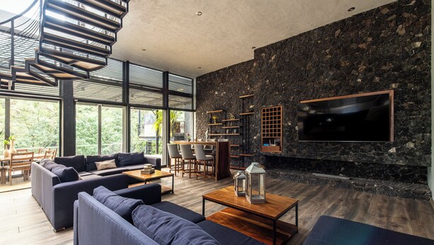 Ein modernes Wohnzimmer mit Wendeltreppe, Steinwand, großem Fernseher und Essbereich mit Holzmöbeln.