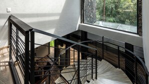 Eine Wendeltreppe mit Metallgeländer, die zu einem Bereich im zweiten Stock führt, der ein großes Fenster mit Blick auf einen Wald hat.