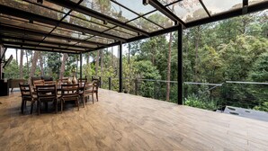 Ein geräumiger Außenbereich zum Essen mit einem Holztisch und Stühlen, umgeben von einer Glasveranda mit Blick auf einen dichten Wald.