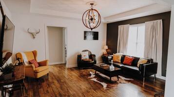 A living room with a wooden floor, a sofa, a coffee table, and a chandelier.