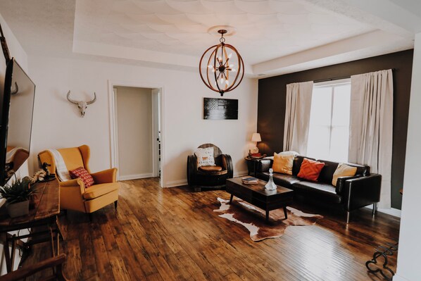 Un salon avec un plancher en bois, un canapé, un fauteuil, une table basse et un lustre.