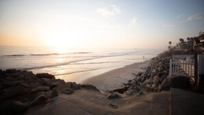 A beach with a rocky shoreline, a white fence, and buildings in the background.