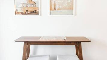 Une table en bois, deux chaises blanches avec des coussins, un tableau encadré au-dessus, et un plancher de couleur claire.