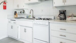 A modern kitchen with white cabinetry, a gas stove, a coffee maker, and a fire extinguisher on the wall.