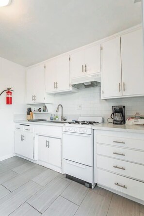 A modern kitchen with white cabinetry, a gas stove, a coffee maker, and a fire extinguisher on the wall. - Spacious 2BR - Patio + Sleeps 6 - Steps to Beach (Oceanside)
