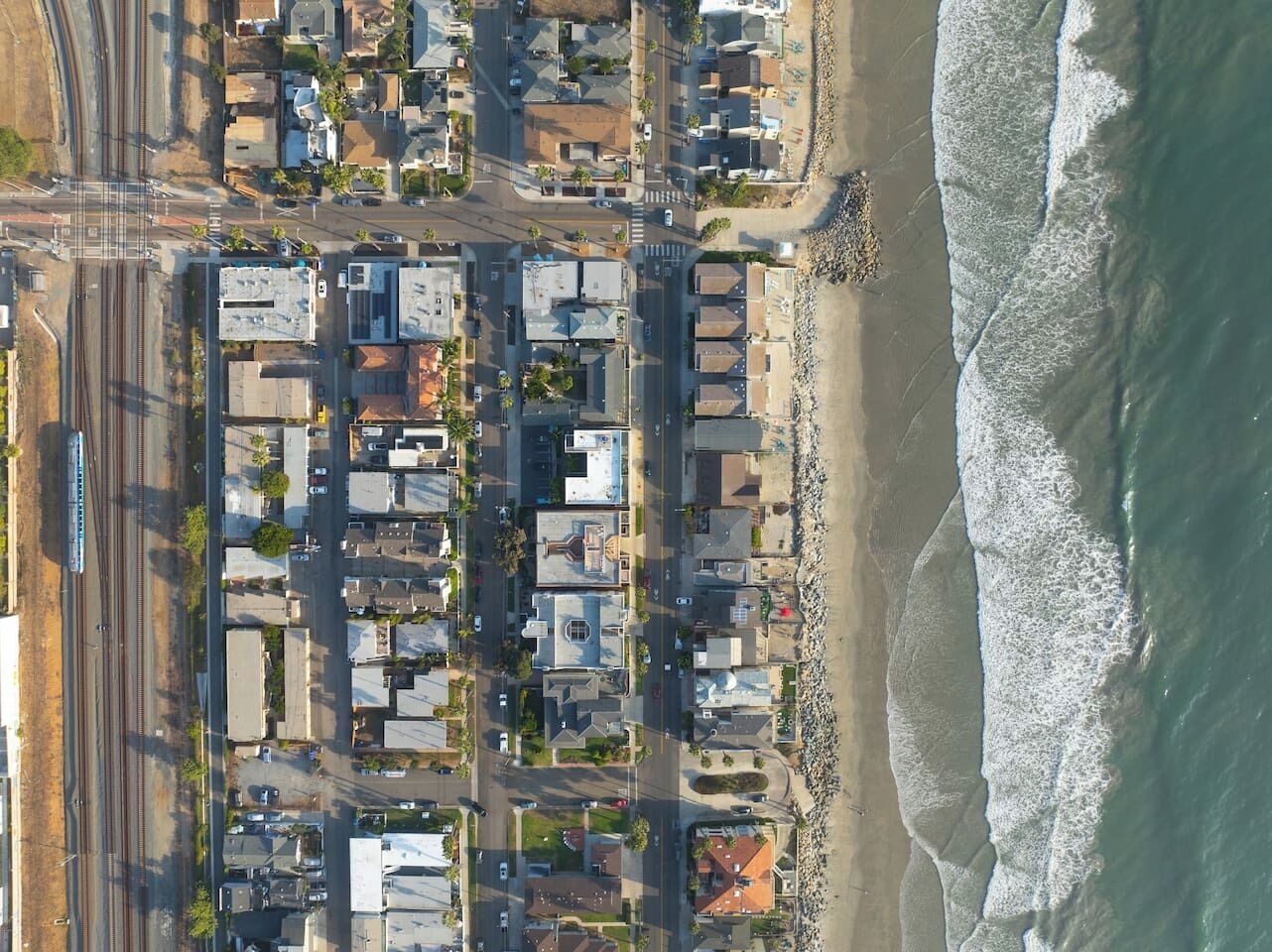 An aerial view of a coastal residential area with houses, a train track, and a beach.