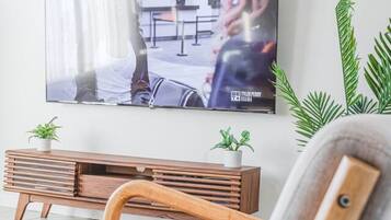 A living room with a television mounted on the wall, a wooden bench, and two potted plants.