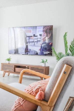 A living room with a television mounted on the wall, a wooden bench, and two potted plants. - Spacious 2BR - Patio + Sleeps 6 - Steps to Beach (Oceanside)