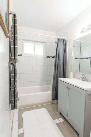 A bathroom with a bathtub, a shower curtain, a sink, and a mirror. - Spacious 2BR - Patio + Sleeps 6 - Steps to Beach (Oceanside)