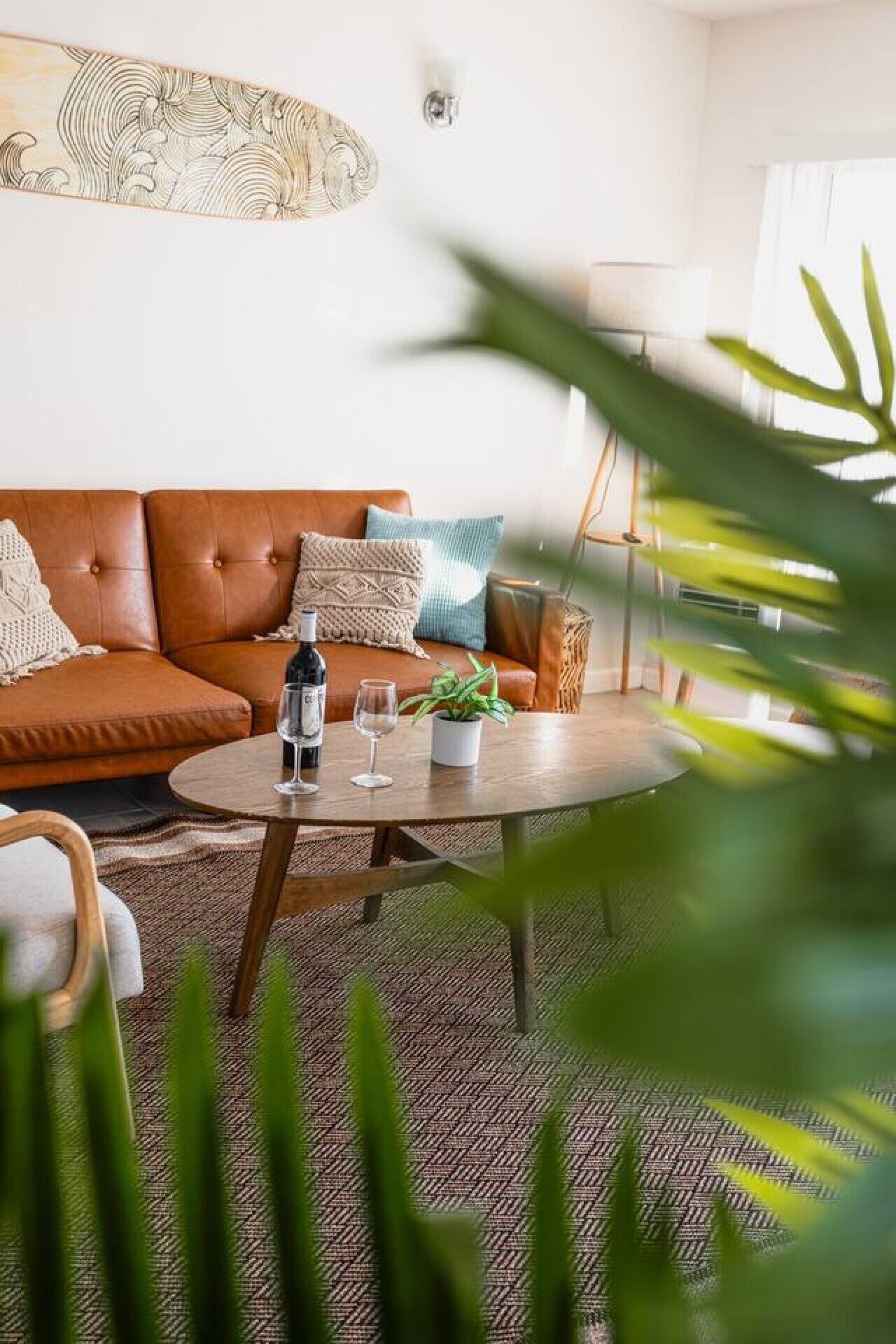 A modern living room with a brown leather sofa, a round coffee table with a wine bottle and glass, and a potted plant.