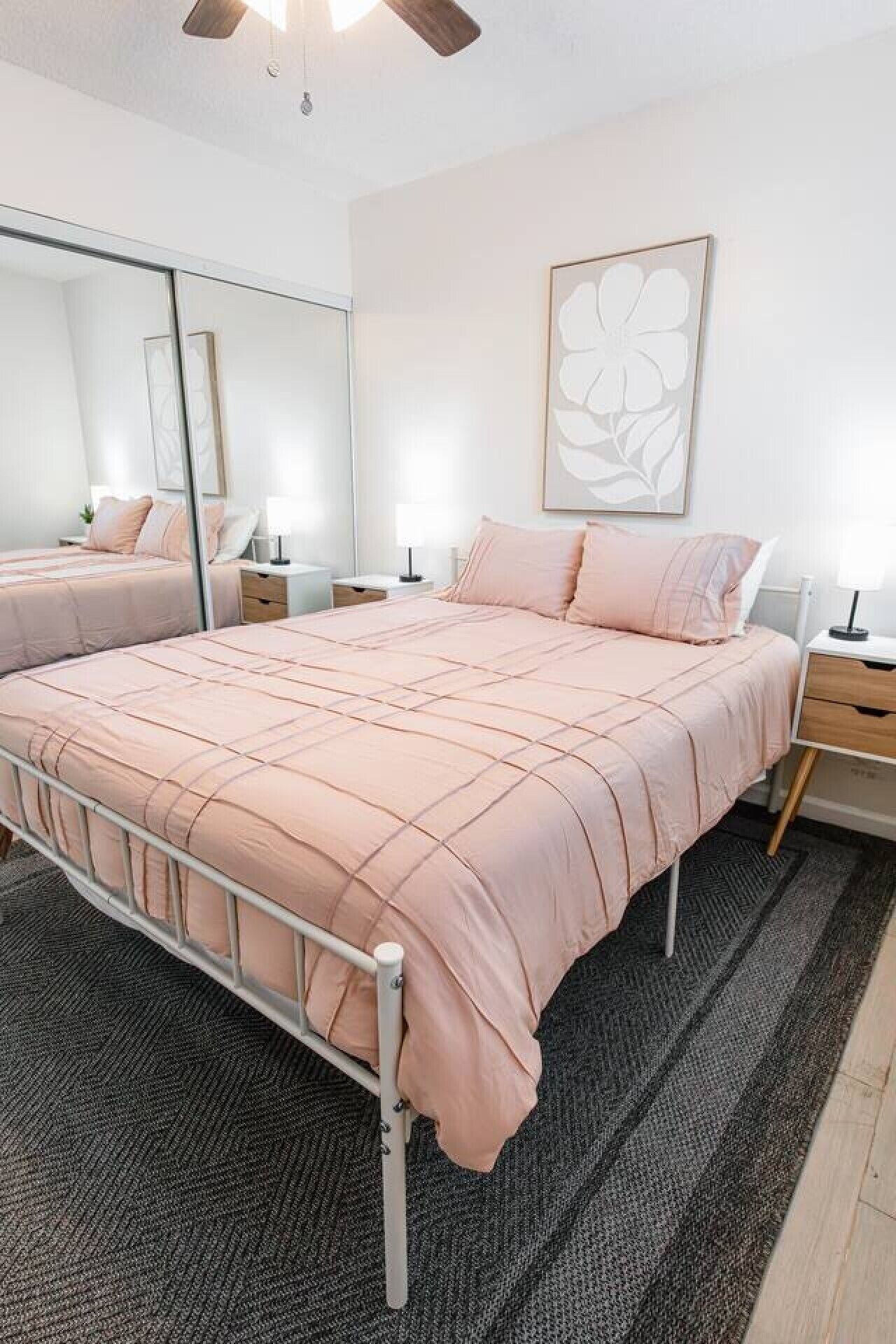 A bedroom with a bed, bedside tables, a mirror, and a wall-mounted artwork.