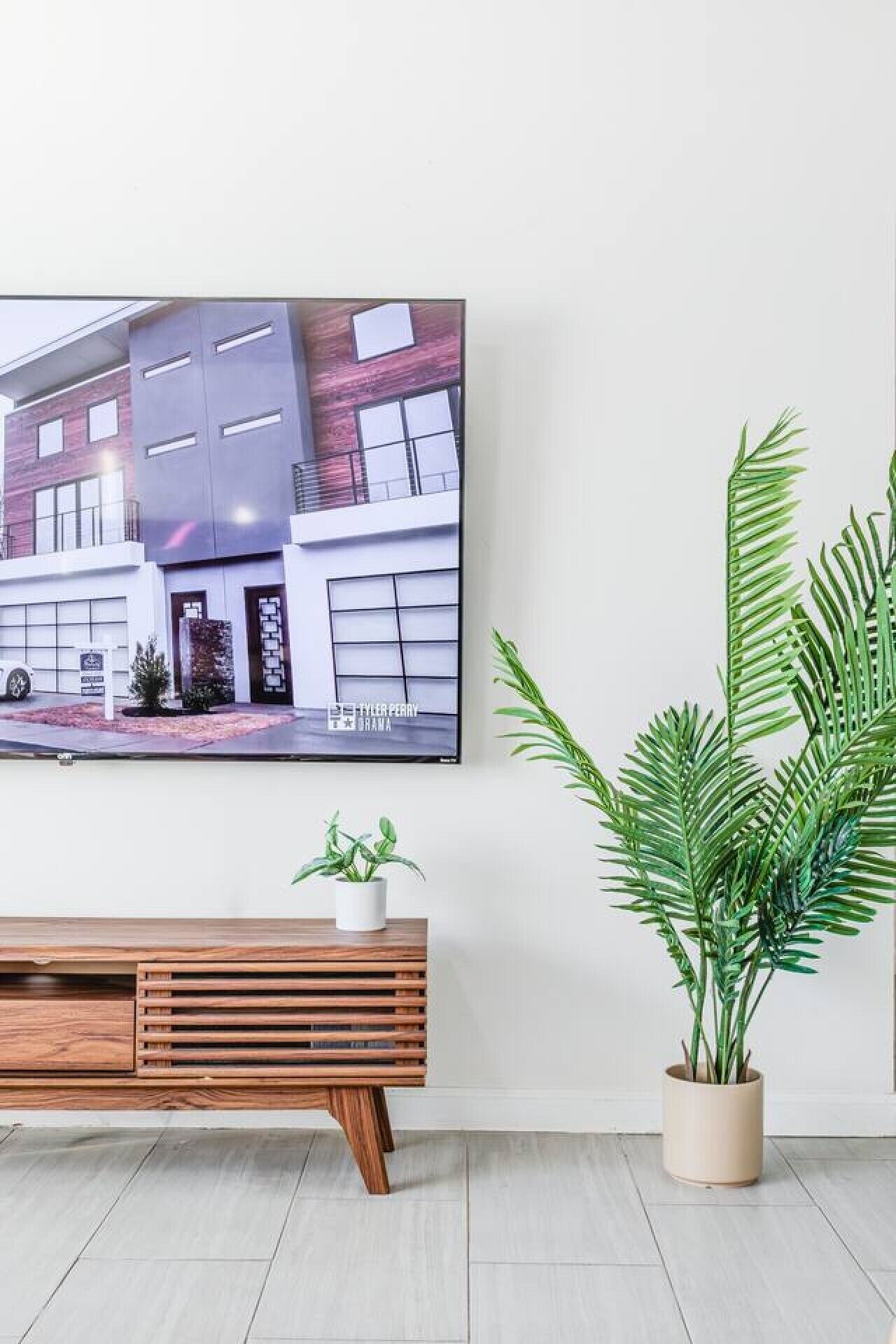 Ein modernes Wohnzimmer mit einem flachbildfernseher an der Wand, einem hölzernen Konsolentisch und einer Topfpflanze.