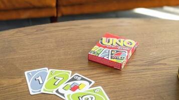 Un canapé en cuir marron agrémenté d’un coussin blanc et bleu, une table basse en bois avec des éléments du jeu UNO, et un jeu de cartes.
