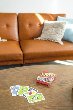 A brown leather sofa with a white and blue pillow, a wooden coffee table with UNO game components, and playing cards.