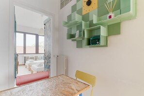 Une chambre d’enfant avec un lit, une table, une chaise et une étagère verte sur laquelle se trouvent une horloge et des objets décoratifs.